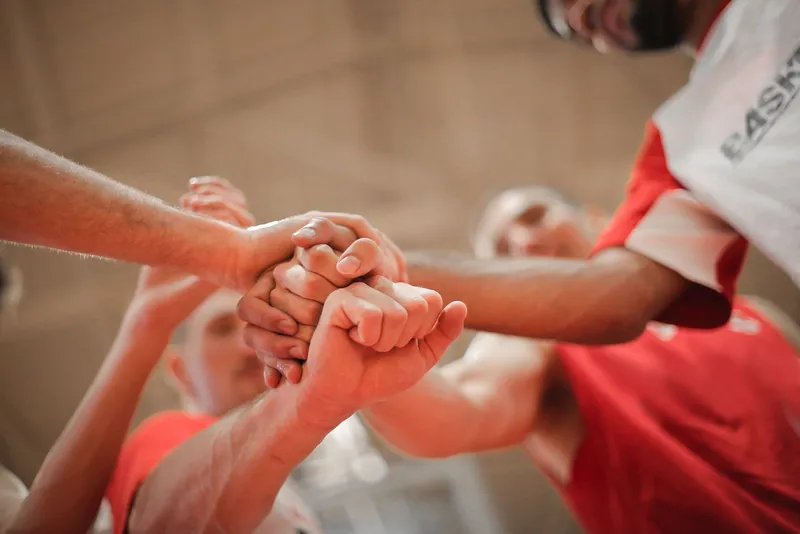 Joueurs de basket en maillot rouge et blanc réunissant leurs mains au centre du cercle, photographiés en contre-plongée.